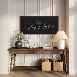 May include: A rectangular wall sign with a black background and a thin wooden frame. The sign features white text that reads: WHATEVER YOU DO, DO IT ALL FOR THE glory of God. The text is displayed in a combination of block and script fonts.
