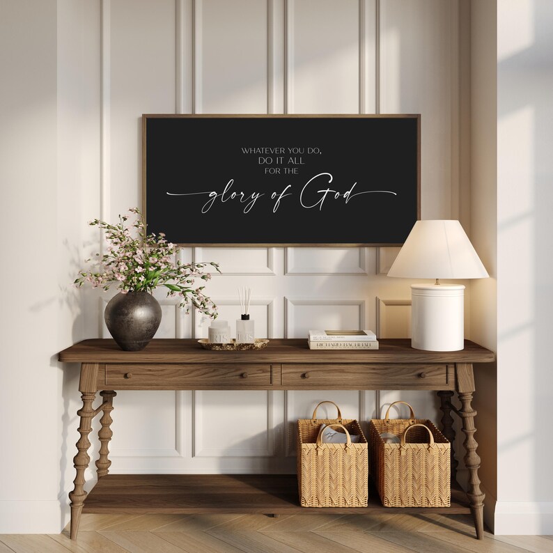 May include: A rectangular wall sign with a black background and a thin wooden frame. The sign features white text that reads: WHATEVER YOU DO, DO IT ALL FOR THE glory of God. The text is displayed in a combination of block and script fonts.