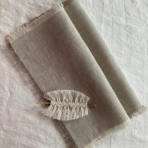 May include: A light brown linen placemat with frayed edges and a white crocheted leaf-shaped ornament on top.