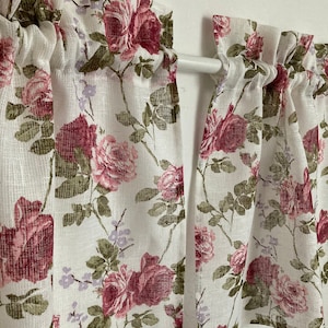 Puede incluir: Un par de cortinas blancas y transparentes con un patrón floral con rosas rosas y rojas. Las cortinas están colgadas en una barra blanca.