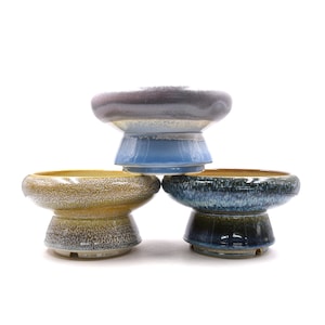 May include: Three ceramic planters in different colors and patterns. The top planter is a light blue and gray color with a speckled pattern. The middle planter is a yellow and brown color with a speckled pattern. The bottom planter is a blue and green color with a speckled pattern.