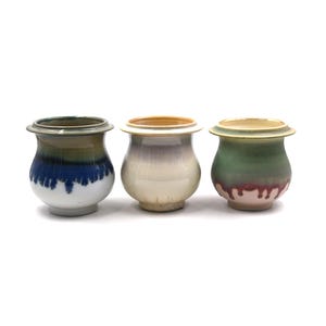May include: Three ceramic pots with a rounded shape and a wide rim. The pots have a variety of colors, including blue, white, green, and purple. The pots are likely for decorative purposes or for holding small plants.