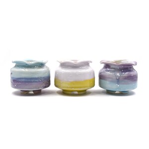 Può includere: Tre vasi di fiori in ceramica con un bordo ondulato e una glassa blu chiaro, giallo e viola. I vasi hanno una finitura macchiata e sono progettati con una base a tre gambe.