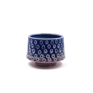 May include: A small, blue ceramic bowl with a textured, teardrop-shaped design. The bowl has a slightly flared rim and a rounded base.