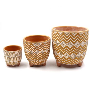 May include: Three yellow ceramic planters with white geometric patterns. The planters have a rounded shape and three small feet.
