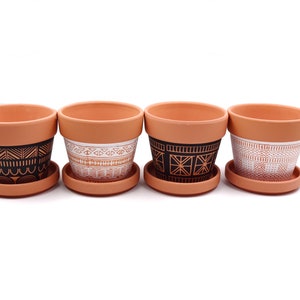 Peut inclure: Quatre pots de fleurs en terre cuite avec des motifs géométriques noirs et blancs. Chaque pot a une soucoupe assortie.