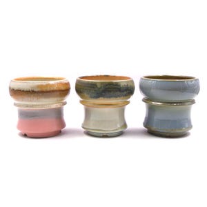 May include: Three ceramic planters with different glaze patterns. The planter on the left has a pink, white, and brown glaze. The planter in the middle has a white, brown, and blue glaze. The planter on the right has a blue and white glaze.