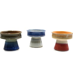 May include: Three ceramic pedestal bowls. Each bowl has a wide, shallow top and a flared base. The colours are blue, brown, and orange with white and red accents. These bowls are likely for serving or display.