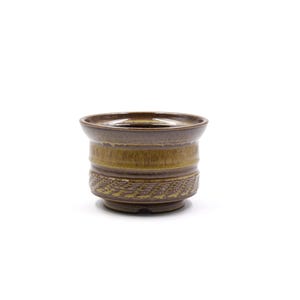 May include: A ceramic planter with a brown and yellow glaze. The planter has a wide, slightly flared rim and a textured band around the base. The design is suitable for small plants and succulents.