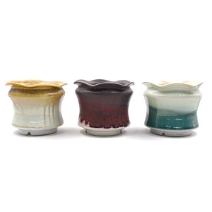 May include: Three ceramic flower pots with a scalloped rim. The pots are glazed in different colors: yellow, brown, and green.