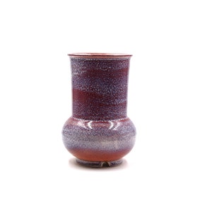 May include: A red and white ceramic vase with a speckled glaze. The vase has a rounded base and a cylindrical neck.