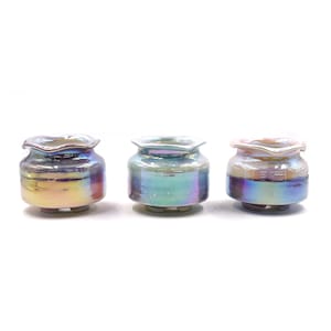 May include: Three iridescent ceramic pots with a pearlescent finish. Each pot has a ruffled rim and sits on three small feet. The colors shift from gold to blue and purple, creating a shimmering effect. These decorative pots are ideal for small plants or succulents.