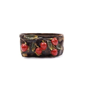May include: A brown ceramic planter with a raised design of a tree branch with red cherries. The planter is oval shaped and has a rustic look.