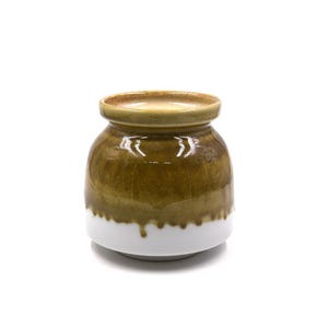 May include: A ceramic jar with a rounded body and a lid. The jar is primarily olive green with a white base. The glaze has a glossy finish. The jar has a ribbed texture around the body.