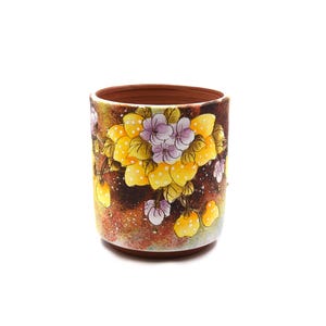 May include: A cylindrical ceramic cup with a terracotta interior and a hand-painted exterior featuring clusters of yellow lemons and light purple flowers against a dark, mottled brown background with white speckles and green foliage accents.