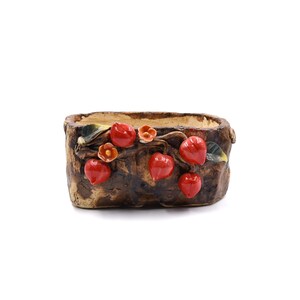 May include: A brown ceramic planter shaped like a tree trunk with red and orange flowers and leaves. The planter is oval shaped and has a rustic look.