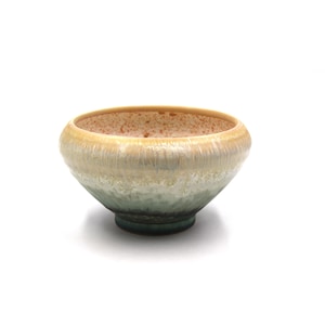May include: A ceramic bowl with a rounded shape and a wide opening. The bowl features a gradient of colors, transitioning from a light tan rim to a pale green midsection and a dark green base. The interior has a speckled, textured appearance.