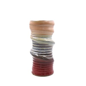 Può includere: Un vaso in ceramica con un designo a spirale multicolore. Il vaso è di colore pesca chiaro nella parte superiore, passando al blu chiaro e poi al viola scuro nella parte inferiore.