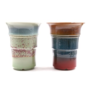 May include: Two ceramic planters with a layered glaze design. The planter on the left has a green, blue, and white glaze. The planter on the right has a brown, blue, and red glaze.