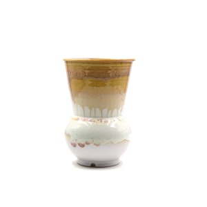 Pode incluir: Um vaso de cerâmica branco com uma base larga e uma abertura estreita. O vaso tem um esmalte amarelo e laranja com um efeito de gotejamento branco.