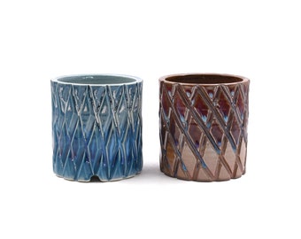May include: Two ceramic planters with a diamond pattern. The planter on the left is blue and the planter on the right is brown.