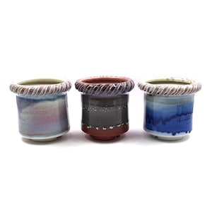 May include: Three ceramic pots with different colored glazes. The pots have a textured rim and are all different sizes.