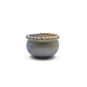 Pode incluir: Um vaso pequeno, redondo, de cerâmica azul claro com um design de corda dourada em torno da borda. O vaso é perfeito para plantas pequenas ou suculentas.