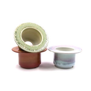 May include: Three ceramic planters in different colors and glazes. The top planter is green with white speckles, the middle planter is brown, and the bottom planter is light blue with purple streaks.