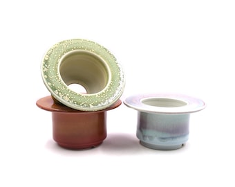 May include: Three ceramic planters in different colors and glazes. The top planter is green with white speckles, the middle planter is brown, and the bottom planter is light blue with purple streaks.