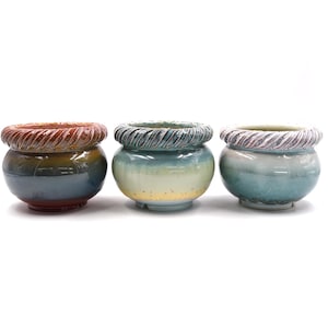 Pode incluir: Três vasos de flores de cerâmica com um design de corda em torno da borda. Os vasos são em tons de azul, verde e marrom.