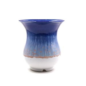 Puede incluir: Un jarrón de cerámica azul y blanco con un borde acampanado y una base redondeada. El jarrón tiene un degradado de colores azules con una base blanca y un diseño moteado marrón claro.