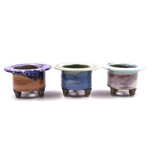 May include: Three small ceramic pots with a wide rim and three legs. The pots are glazed in different colors, including blue, green, and purple.