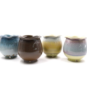 May include: Four ceramic flower pots in different colours and patterns. The pots have a scalloped rim and a rounded body. The colours are blue, brown, yellow, and purple.