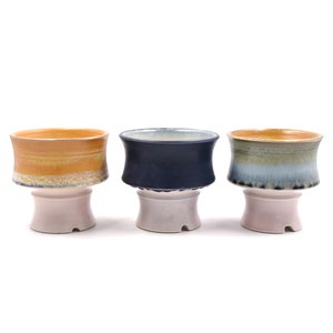 May include: Three ceramic planters with a light pink base and a glazed top. The planters are in different colors: yellow, blue, and green.
