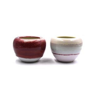 May include: Two small ceramic pots, one with a red and white glaze and the other with a white, gray, and pink glaze.