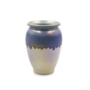 May include: A small, handcrafted ceramic vase with a rounded body and a slightly flared rim. The vase features a gradient of colors, transitioning from a deep blue at the top to a pale, iridescent cream at the base. The rim is a metallic silver color.