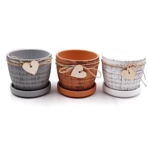 May include: Three terracotta plant pots with a rustic, textured finish. Each pot has a jute twine bow with a wooden heart charm.