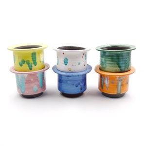 May include: Four ceramic planters with colorful abstract designs. The planters are stacked in pairs, with the top planter of each pair being a lighter color than the bottom planter. The planters are all different colors, including yellow, green, blue, and orange.