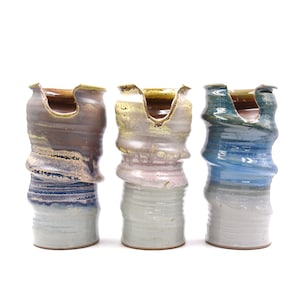 Pode incluir: Três vasos de cerâmica com um design ondulado único. Os vasos são envidraçados em tons de marrom, rosa e azul.