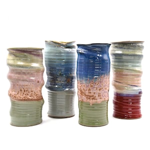 Może przedstawiać: Cztery ceramiczne wazony o falistym, fakturowanym wzorze. Wazony są w odcieniach niebieskiego, zielonego, różowego i czerwonego.