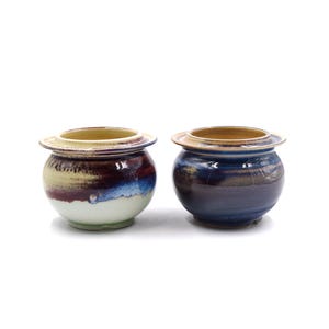 May include: Two ceramic pots with a glazed finish. The pot on the left has a white, yellow, and purple glaze. The pot on the right has a blue, purple, and brown glaze.