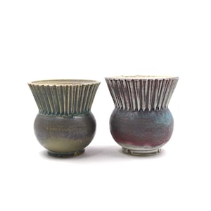 Pode incluir: Dois vasos de cerâmica com uma borda texturizada e canelada. O vaso à esquerda é verde e castanho, enquanto o vaso à direita é roxo e azul.