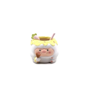May include: A white ceramic planter shaped like a pig wearing a costume with a yellow frosting-like rim decorated with sprinkles. The pig has a pink snout, small black eyes, and holds a small carrot-shaped accessory near its face.