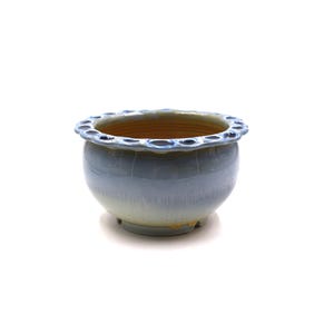 May include: A round ceramic planter with a glossy light blue glaze that fades into a pale cream base. The rim features a decorative scalloped edge with small circular indentations. The interior of the bowl is a warm, unglazed tan color.