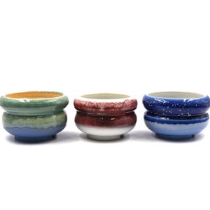May include: Three ceramic pots in shades of green, red, and blue. Each pot has a rounded rim and a contrasting base color. The green pot has a gradient effect, while the blue pot has white speckles.