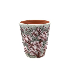 May include: A tapered ceramic plant pot featuring a textured gray and green mottled finish. The exterior is decorated with raised, hand-painted brown branches and clusters of light pink cherry blossom flowers. The interior has a terracotta finish.