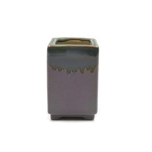 May include: A square ceramic planter with a glossy finish. The planter has a dark purple base with a dark green top and a dripped glaze effect. The planter is designed with a small square base.