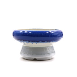 May include: A blue and white ceramic planter with a wide, shallow bowl and a pedestal base. The bowl has a blue glaze with a white rim, and the base is white with a blue glaze.