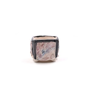 May include: Square ceramic planter with a black rim and colorful painted design. The planter has four small feet.