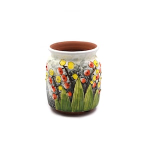 May include: A ceramic vase with a white rim and a brown interior. The exterior is decorated with a floral design featuring yellow and red berries, green leaves, and a gray background. The vase is a decorative item.